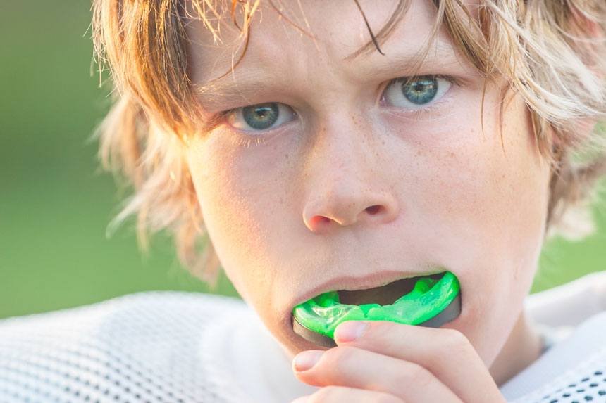 Boy putting on green mouthguard before game