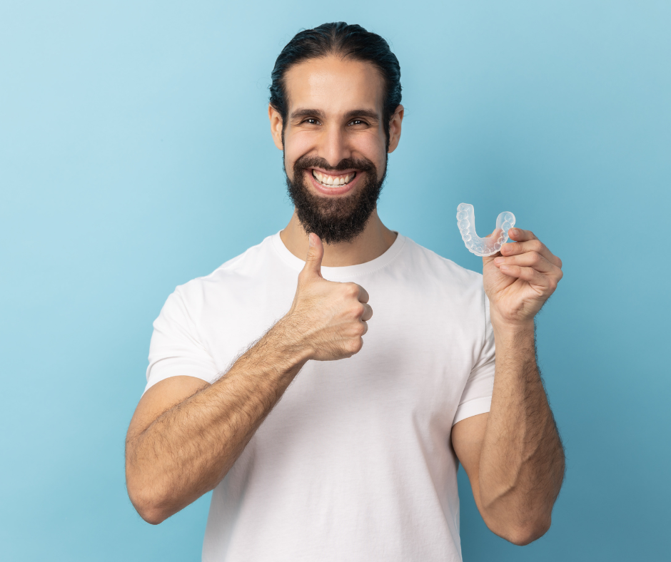 Man smiling, holding dental aligner and thumbs up